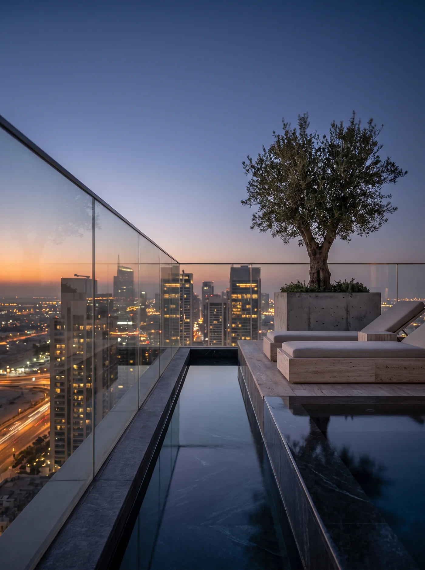 Terrasse eines Penthouses in der Dämmerung mit schmalem Pool und Blick über eine beleuchtete Stadt